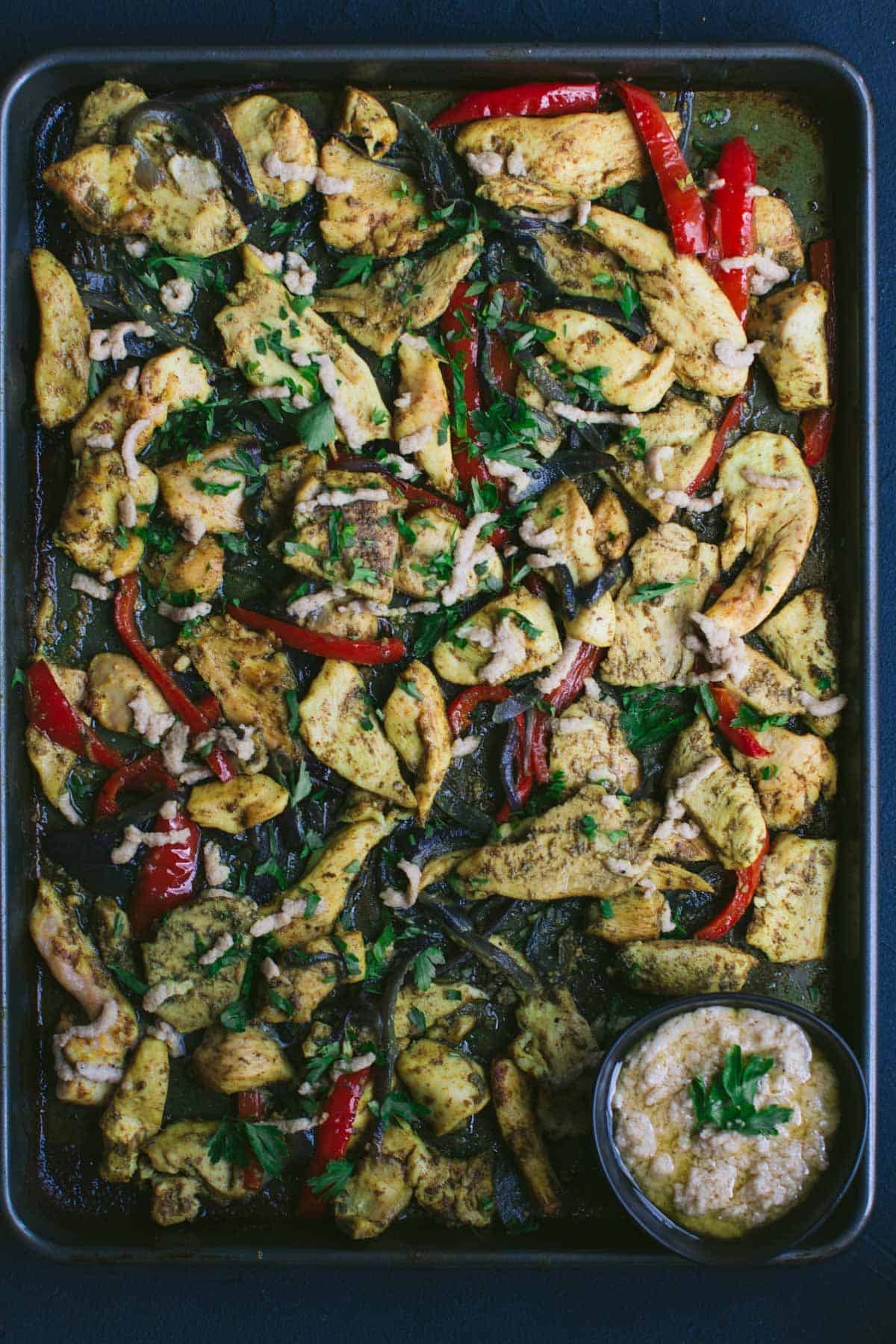 Baked chicken  on a sheet pan with sauce on a bowl