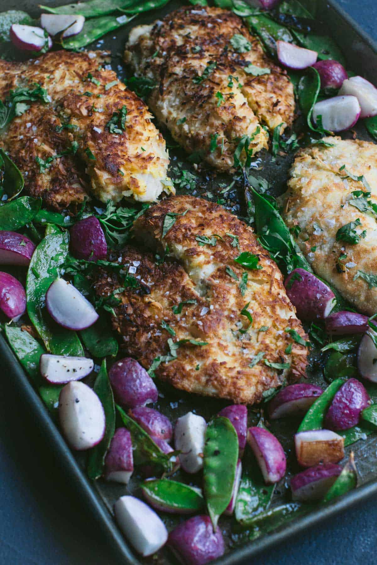 Baked coated fish and veggies on a sheet pan.