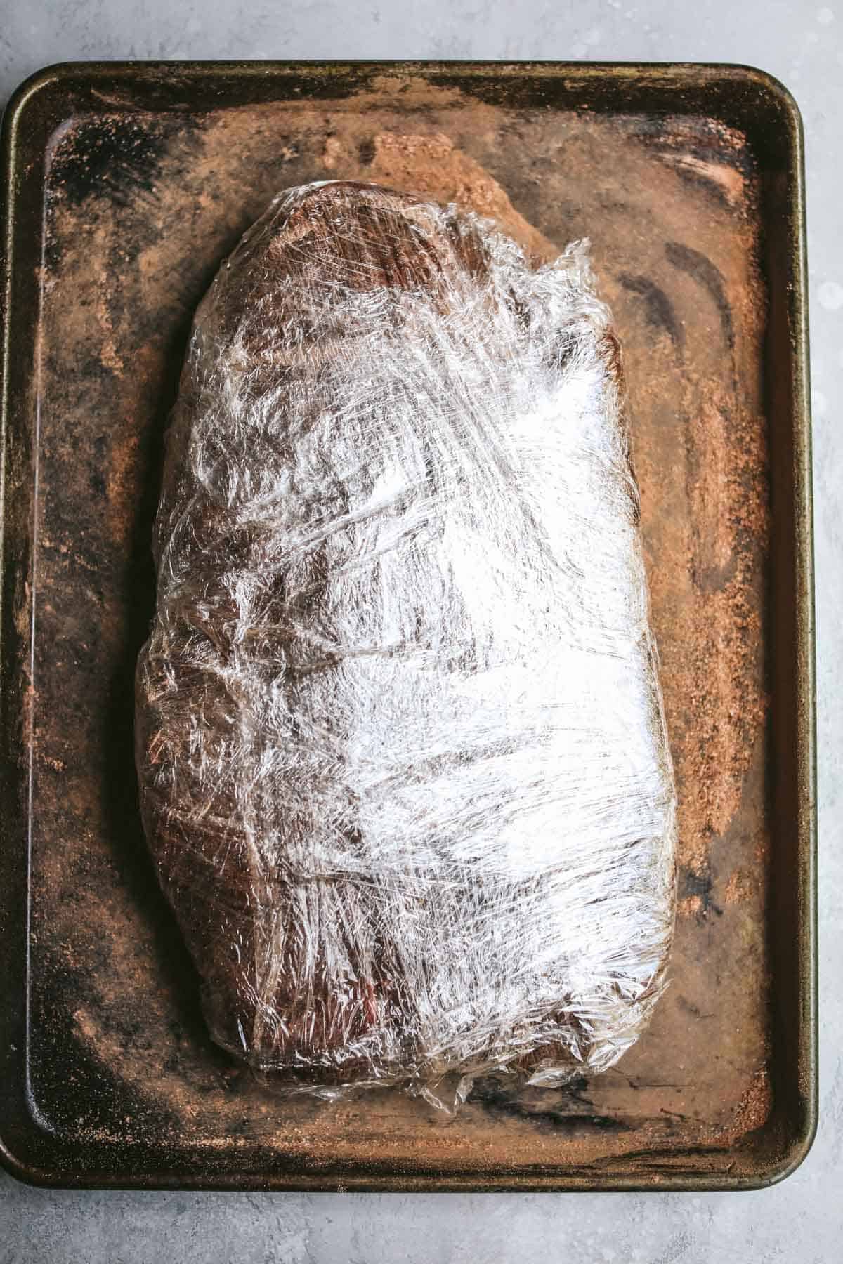 brisket covered in plastic wrap